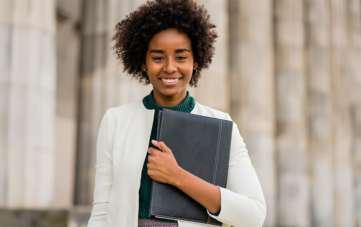 Woman smiling wearing professional dress and holding a padfolio as she learns to navigate the job market as a GenZer.